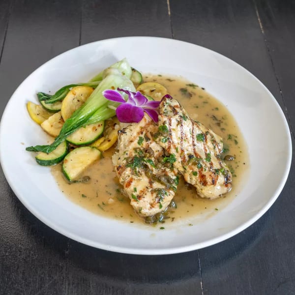 Grilled chicken with capers, herbs, and sauce, served with zucchini, squash, and bok choy.