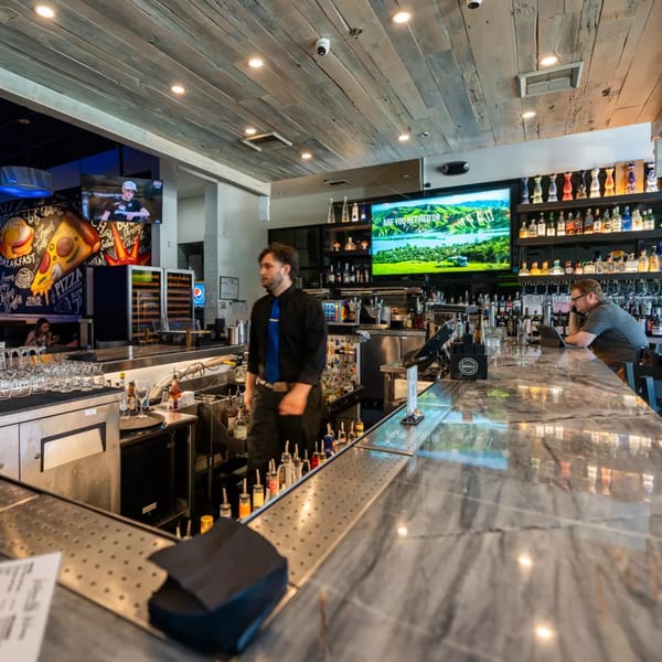 A bartender works behind a long, sleek bar with a customer seated at the far end.