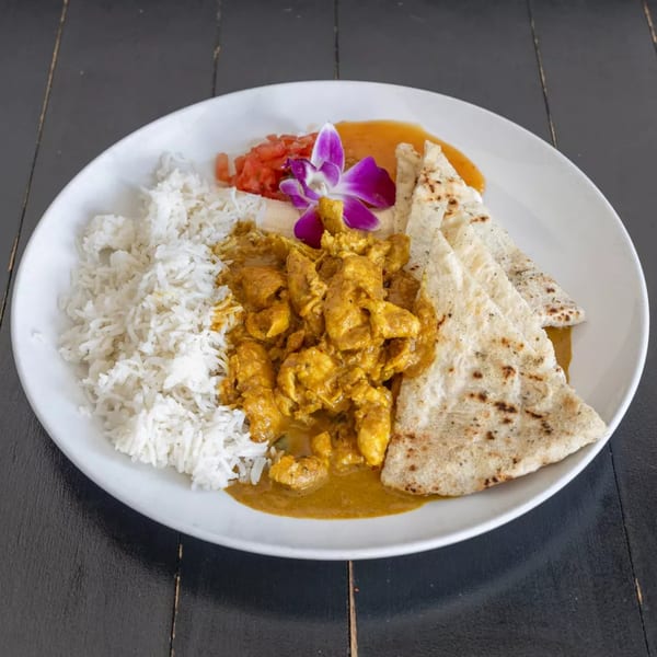 Chicken curry with white rice, flatbread, and a purple orchid garnish on a white plate.
