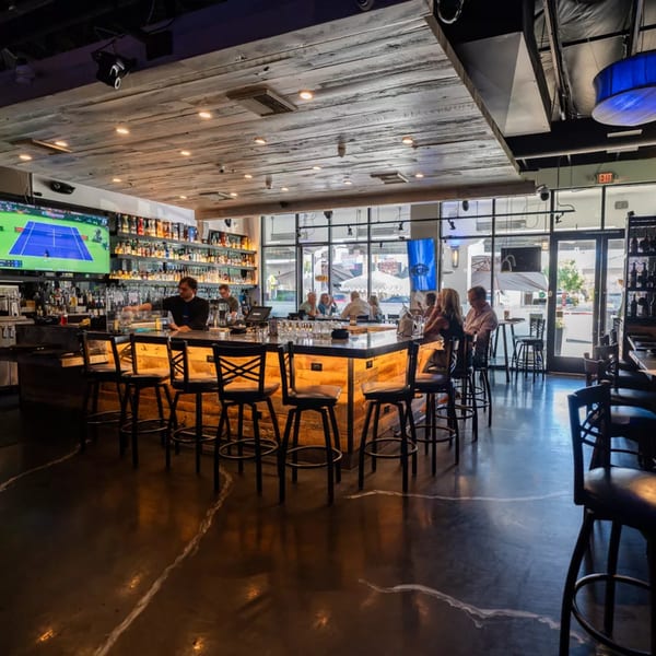 Kitchen 86's lively bar area with patrons, a bartender, and a large selection of spirits.