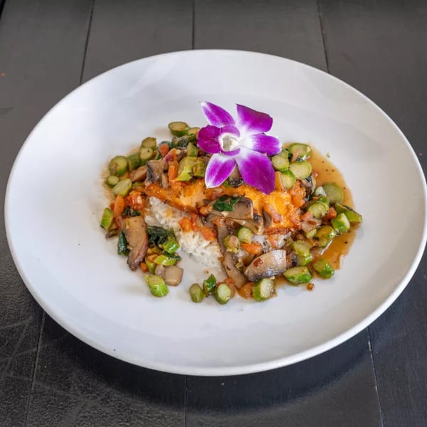 A white plate of Kitchen 86's American cuisine, featuring salmon over rice with vegetables and a purple orchid.