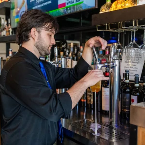 A bartender in a black shirt and blue tie pours a beer from a tap at Kitchen 86.