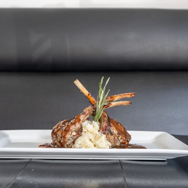 Two lamb chops with mashed potatoes and rosemary sprig on a white rectangular plate.