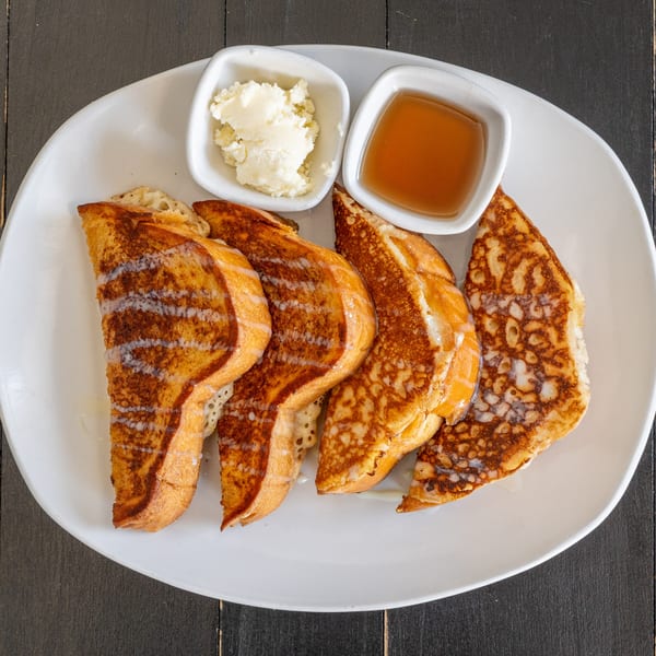 Four pieces of golden-brown French toast with syrup and butter on a white plate.