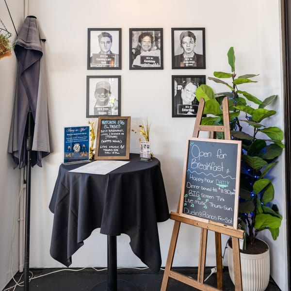 Restaurant entrance with a black tablecloth, chalkboards displaying specials, and framed mugshot-style photos.