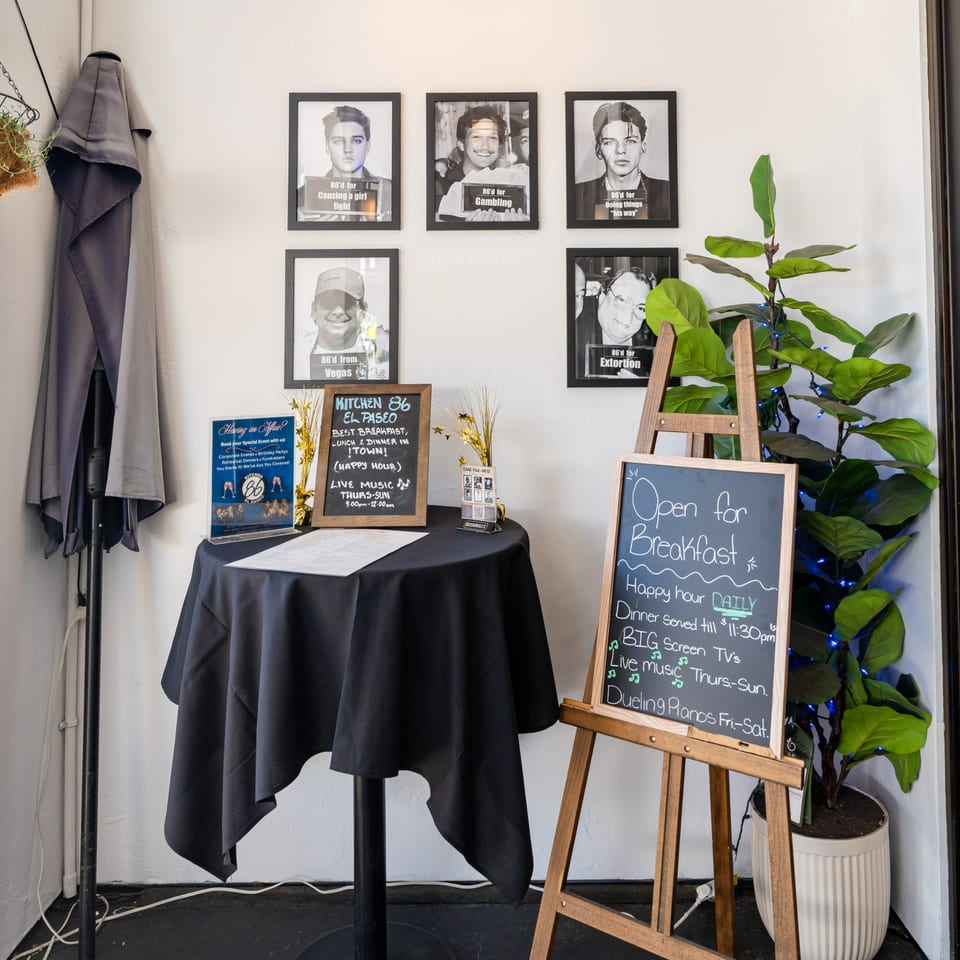Restaurant entrance with a black tablecloth, chalkboards displaying specials, and framed mugshot-style photos.