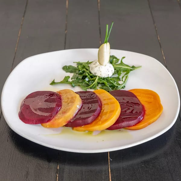 Beetroot carpaccio with arugula, goat cheese, and a pear slice on a white plate.