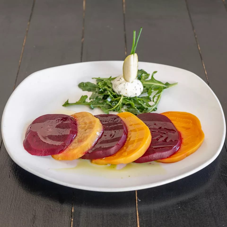 Beetroot carpaccio with arugula, goat cheese, and a pear slice on a white plate.