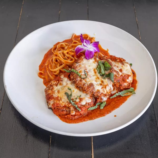 Chicken Parmesan with linguine pasta, red sauce, melted cheese, basil, and an orchid garnish.