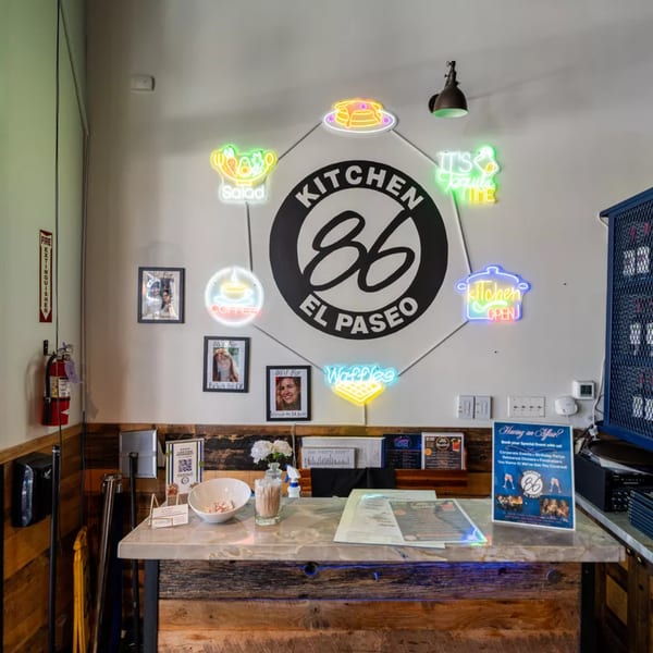 Kitchen 86 El Paseo restaurant interior with a counter and neon signs for coffee, waffles, and salad.