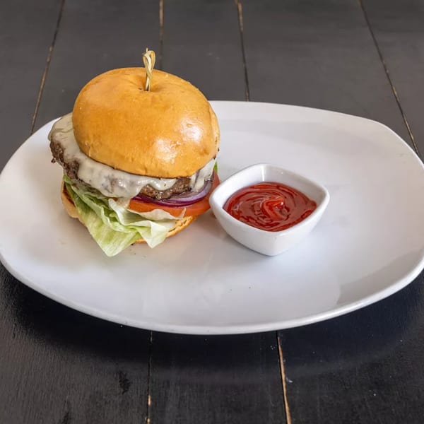A Kitchen 86 cheeseburger with lettuce, tomato, and onion, served with a side of ketchup.