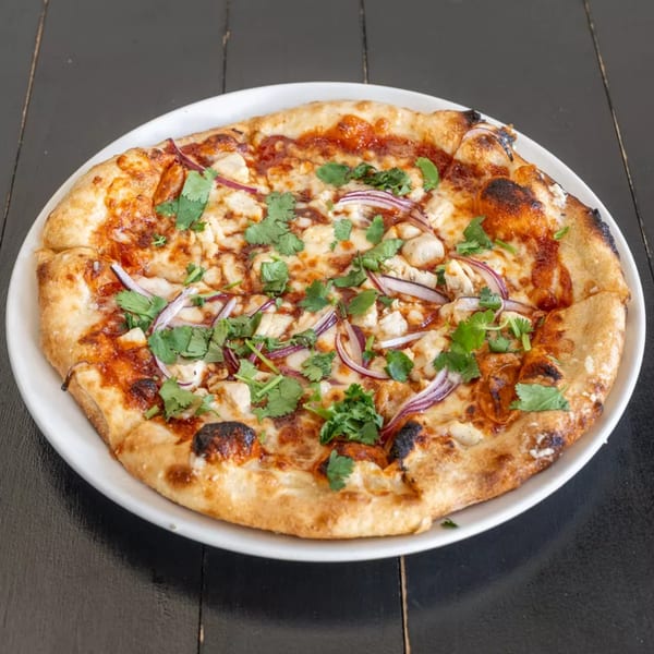 A BBQ chicken pizza from Kitchen 86, topped with red onions and cilantro, on a white plate.